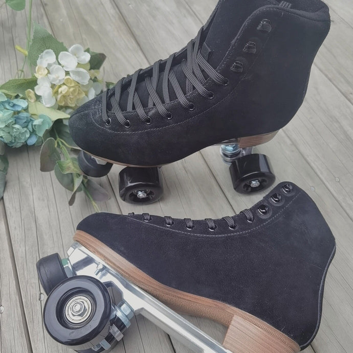 The Seed Project roller skates. colour is Black Robin with black laces on a wooden background surrounded by flowers and leaves.