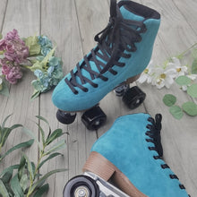 Load image into Gallery viewer, The Seed Project roller skates. Colour is Tui with black laces on a wooden background surrounded by flowers and leaves.
