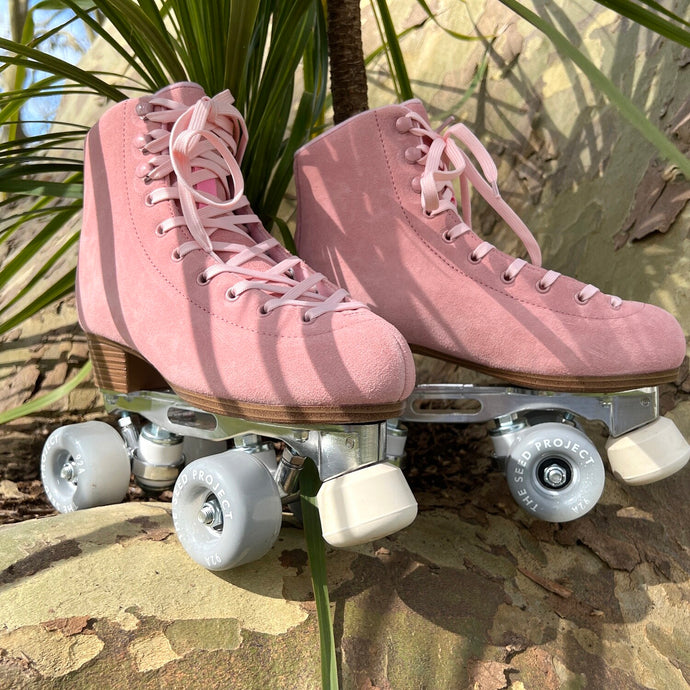The Seed Project SeedPro* roller skates. colour is Galah with light pink laces sitting on a rock infront of a plant