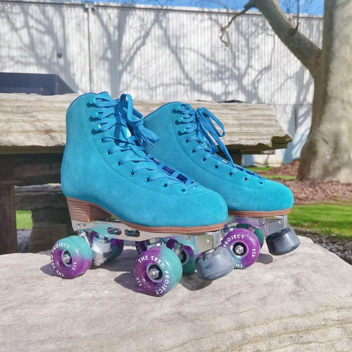 The Seed Project SeedPro* roller skates with turquoise laces sitting on a rock in a park.